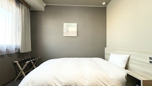A hotel room with a large bed, a small bedside table, a wall-mounted air conditioner, and a window with sheer curtains.