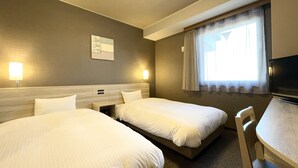 A hotel room with two beds, a desk, a chair, a TV, and a window with curtains.