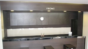 Un comptoir d’accueil surmonté d’une enseigne indiquant « ENTRÉE », deux tabourets en bois et une petite table placée devant.
