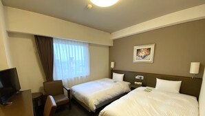 Une chambre d’hôtel avec deux lits, un bureau, une chaise, une télévision et une fenêtre avec des rideaux.