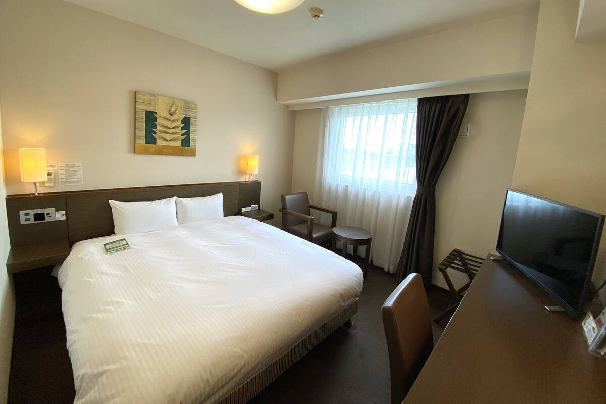 A hotel room with a large bed, a desk with a television, a small table, and a chair.