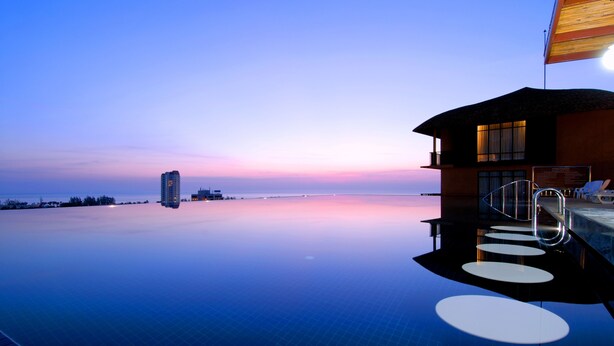 A modern infinity pool with a clear view of the ocean and a building with a balcony. - Karon Phunaka Resort (Karon)