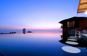 Una piscina infinita moderna con vista despejada al océano y un edificio con balcón.