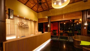 A reception area with a wooden reception desk, a ceiling fan, and a seating area with wicker furniture. - Karon Phunaka Resort (Karon)