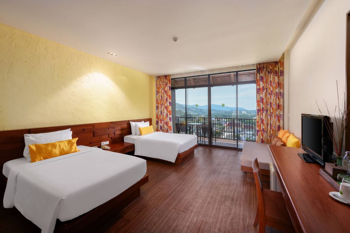Une chambre d’hôtel avec deux lits, un bureau avec une télévision et un balcon avec vue.