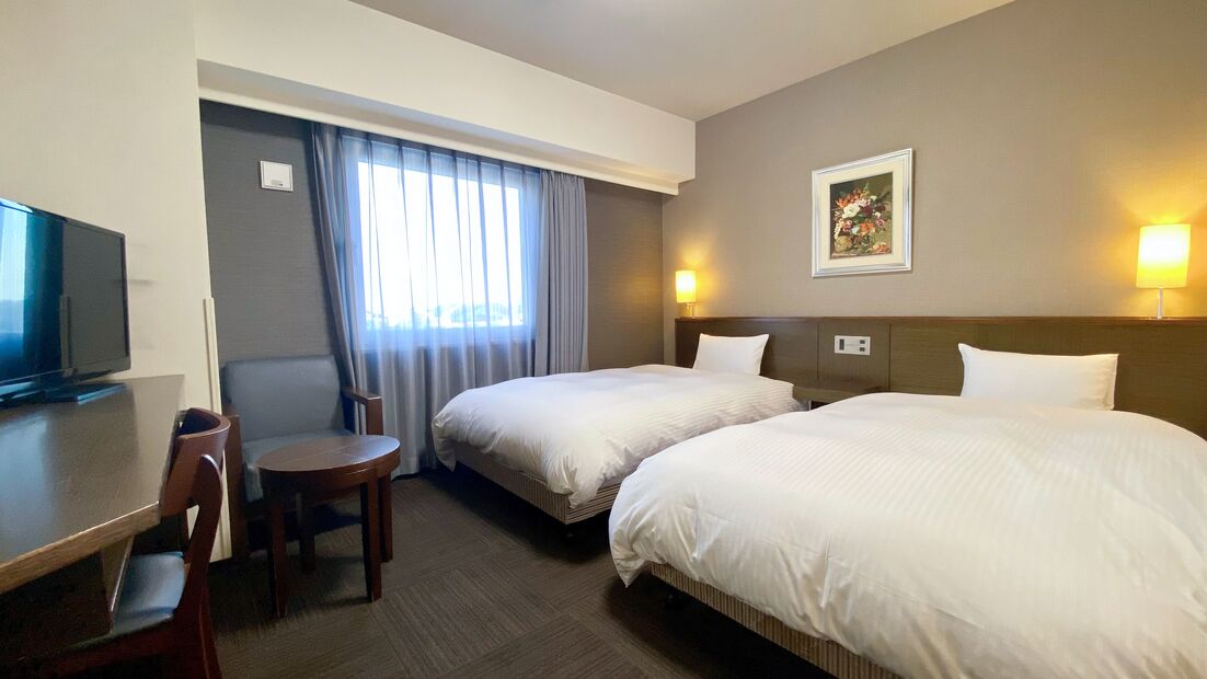 Una habitación de hotel con dos camas, un escritorio con silla, un televisor y un cuadro en la pared.