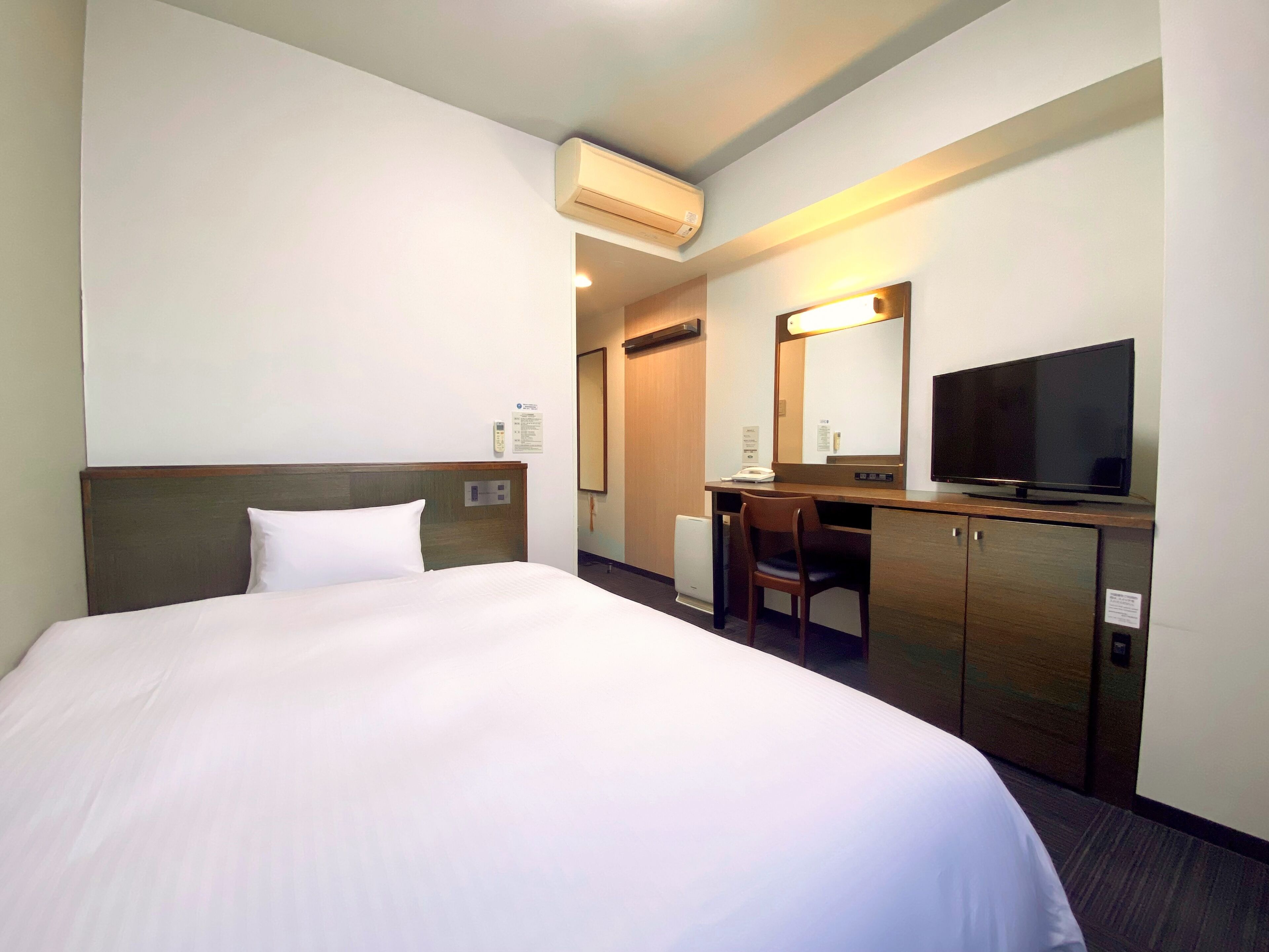 A hotel room with a bed, a desk, a chair, a television, and an air conditioning unit.