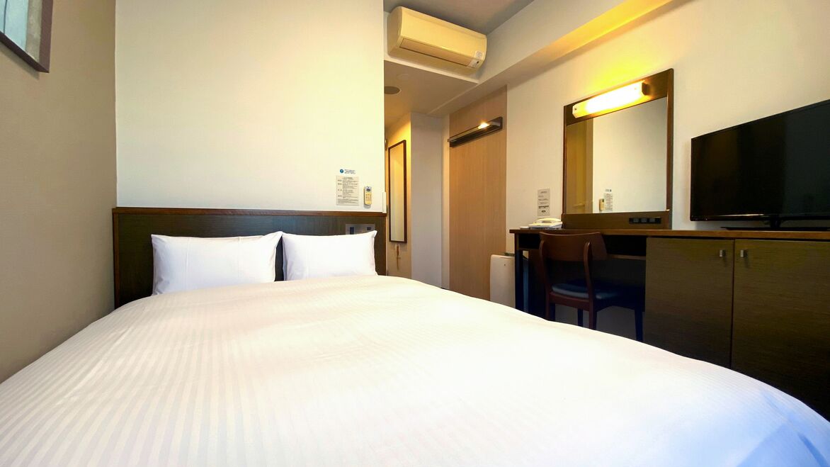 Una habitación de hotel con una cama, un escritorio, una silla, un televisor y un espejo.