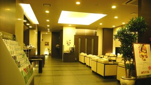 A hotel lobby with a reception desk, seating area, and a large potted plant.