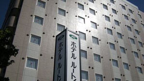 A hotel building with multiple floors, featuring a grid of windows and a prominent vertical sign with Japanese text.