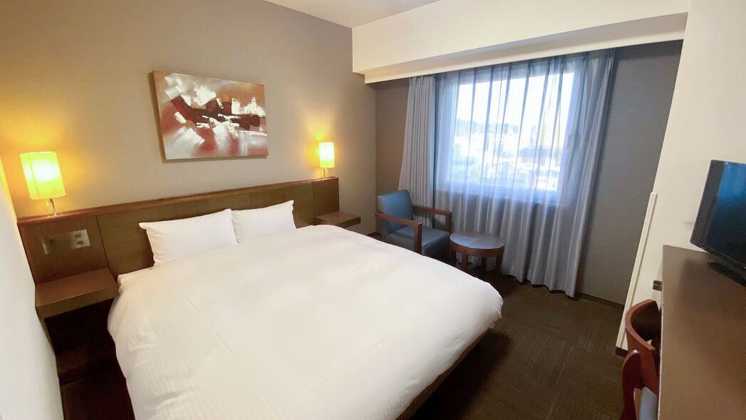 Habitación de hotel con una cama grande, dos lámparas de noche, una silla, una mesita y un televisor.