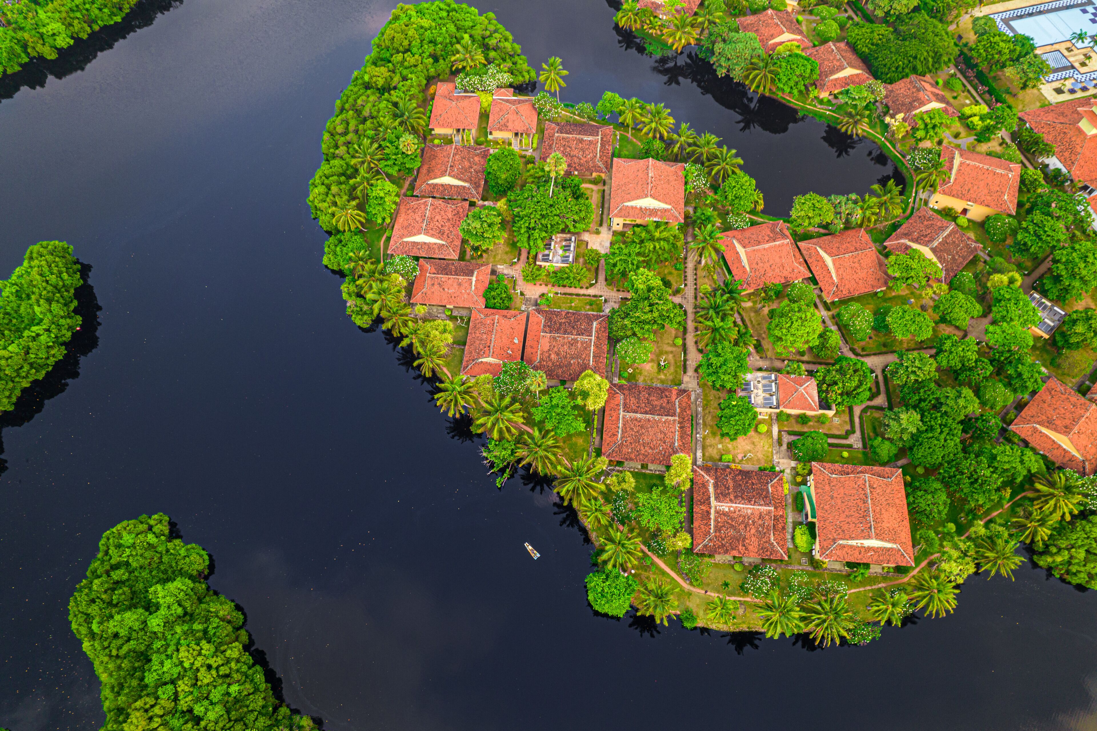 Vue aérienne d’une île tropicale avec plusieurs bâtiments aux toits rouges, entourés d’une végétation luxuriante et de palmiers.