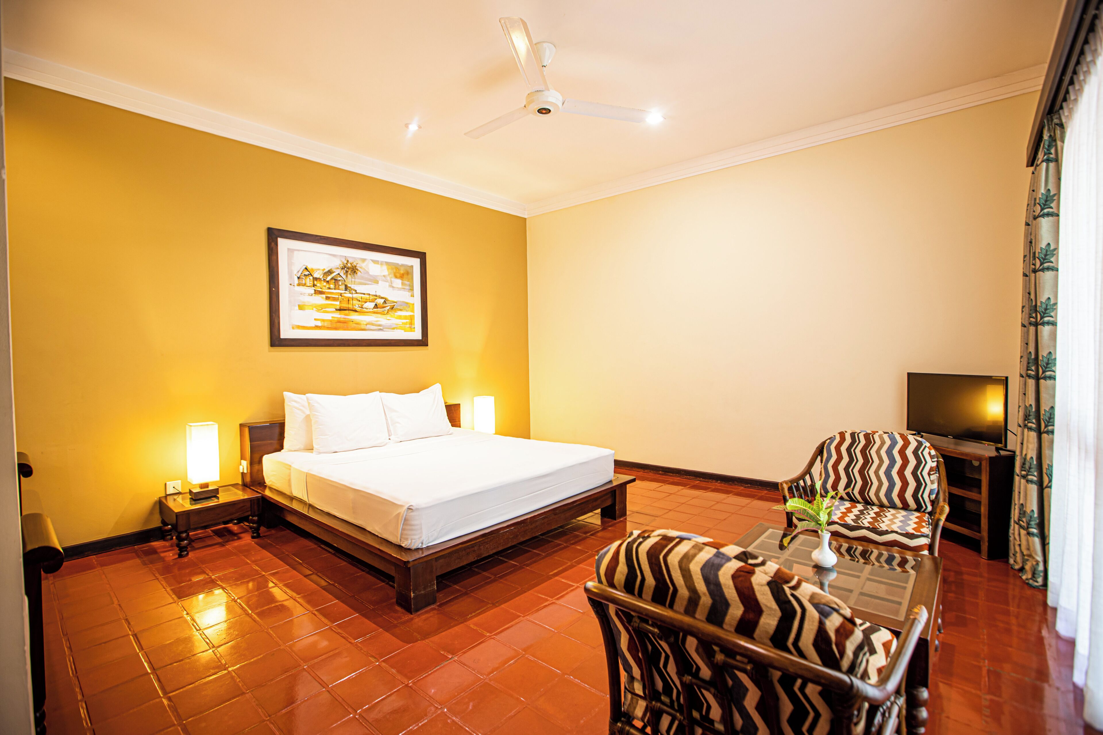 A hotel room with a bed, a chair, a television, and a painting on the wall.