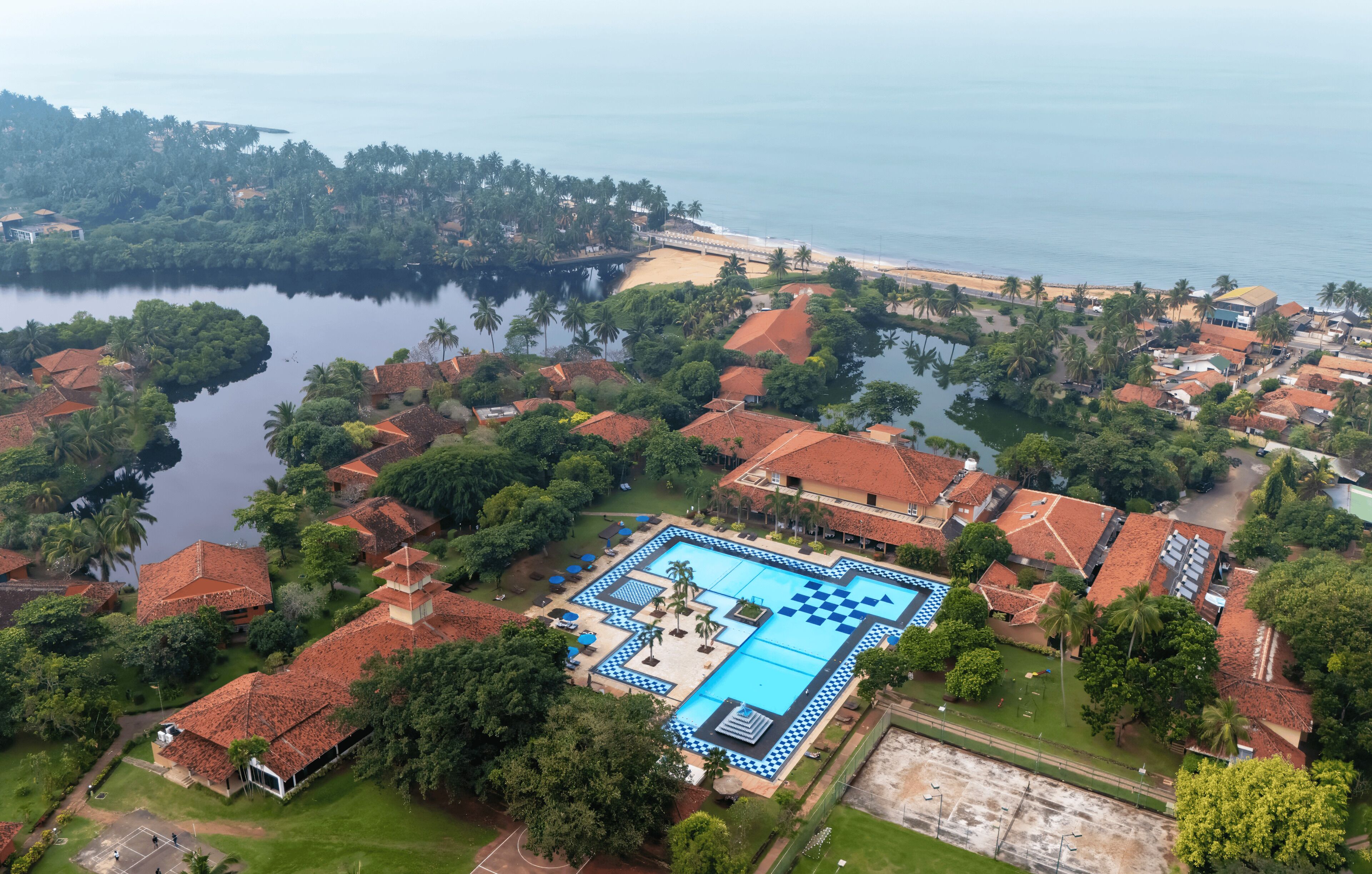 Vista aérea de un resort con una gran piscina, rodeado de exuberante vegetación y una playa.