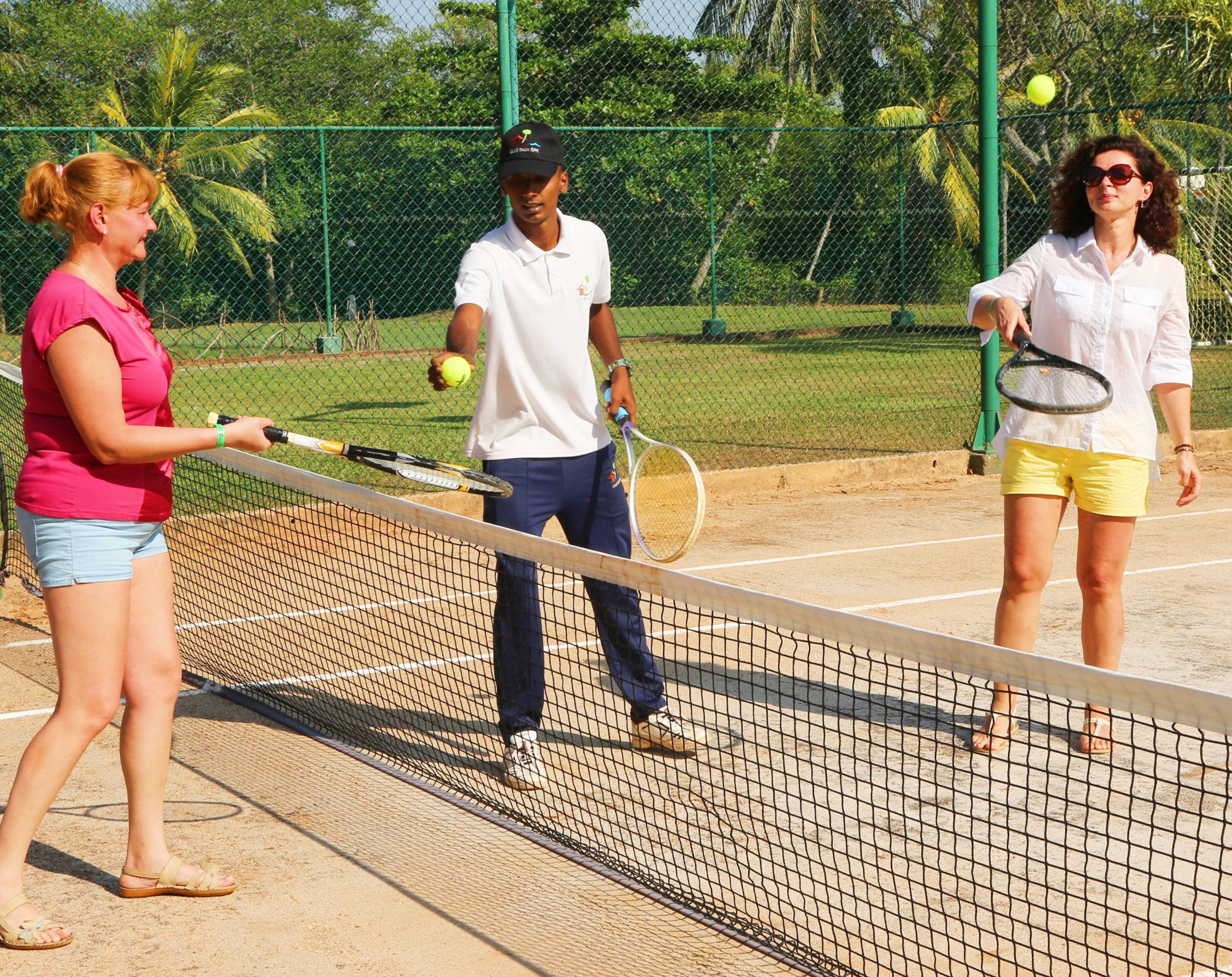 Cancha de tenis con tres personas, una red y una valla.