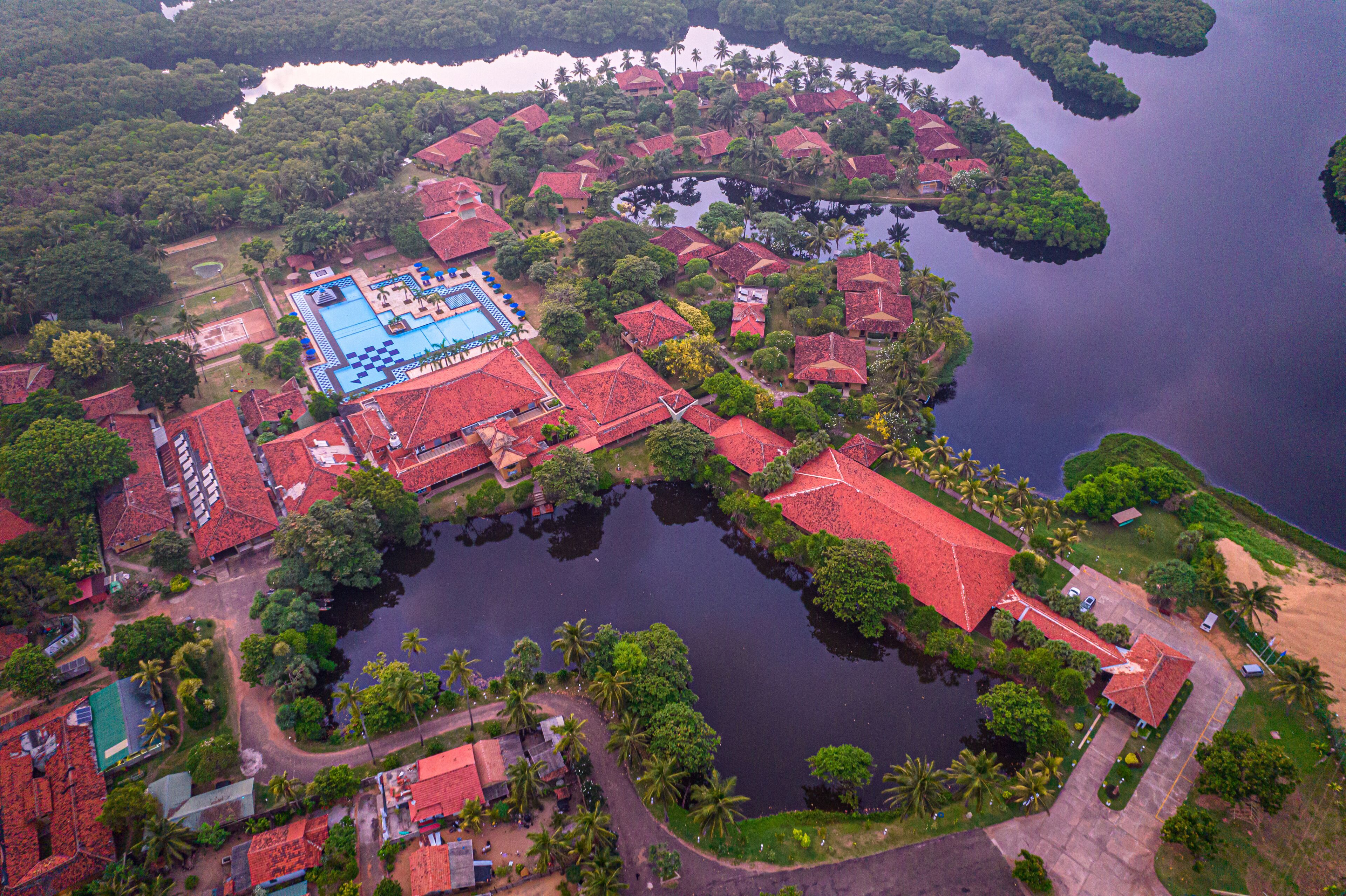 An aerial view of a resort with multiple buildings, a central swimming pool, and surrounding water bodies.