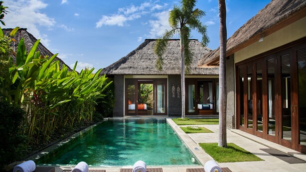 A pool area with lounge chairs and towels, surrounded by tropical plants and a thatched-roof building. - Mahagiri Villas Sanur (Denpasar)