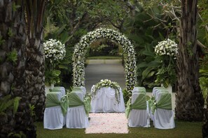Une arche décorative pour cérémonie de mariage installée en plein air, ornée de fleurs blanches et de verdure, et entourée de chaises aux accents blancs et verts.