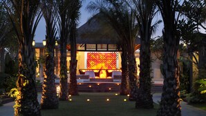 A resort with a central building featuring a large illuminated wall, surrounded by palm trees and a well-maintained lawn. - Mahagiri Villas Sanur (Denpasar)