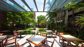 Patio esterno con tavoli e sedie, immerso nel verde e dotato di tetto in vetro.