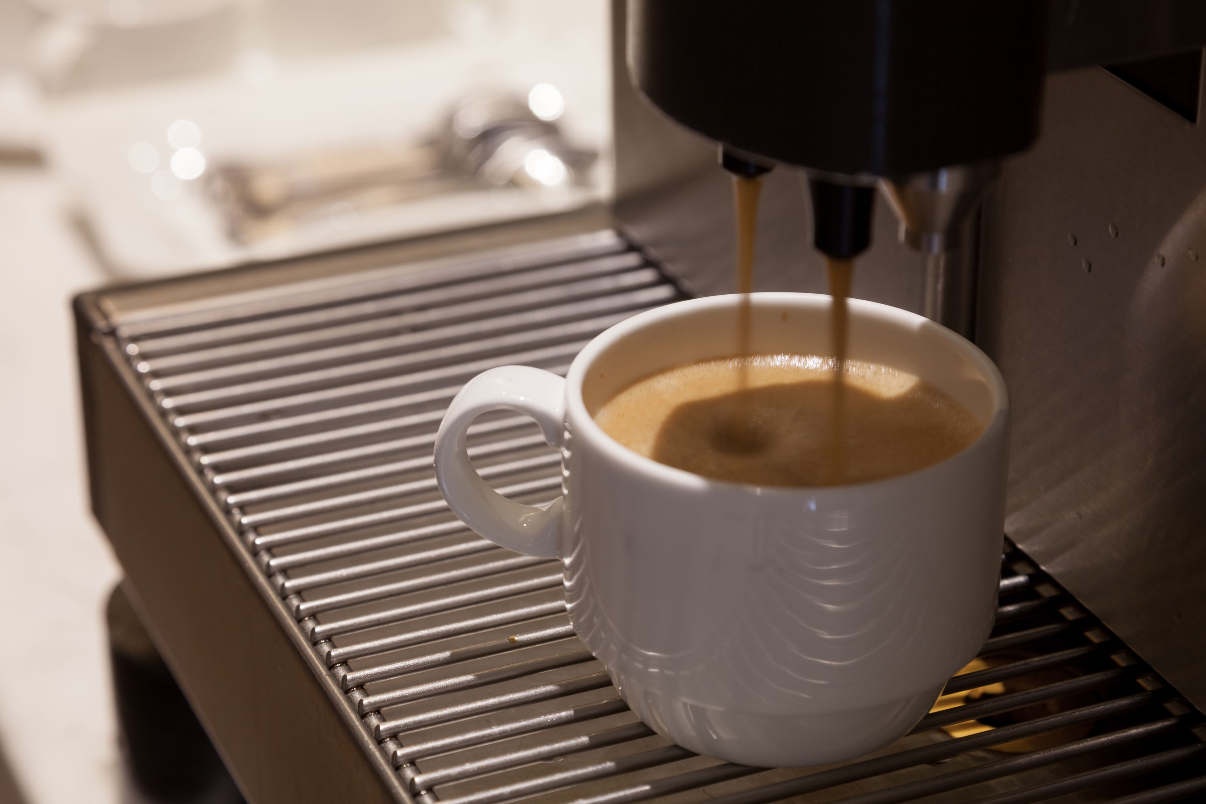 Una tassa de cafè blanca sobre un safata metàl·lica, mentre se'n serveix a dins.