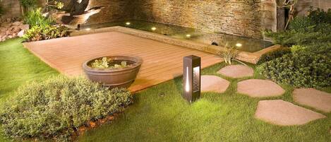 A well-maintained garden with a wooden deck, a stone wall, and a water feature.