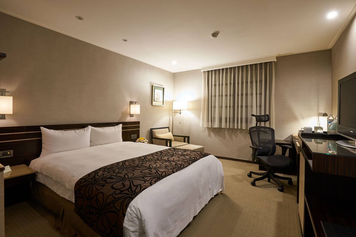 Habitación de hotel con una cama grande, un escritorio con computadora, una silla y un televisor.
