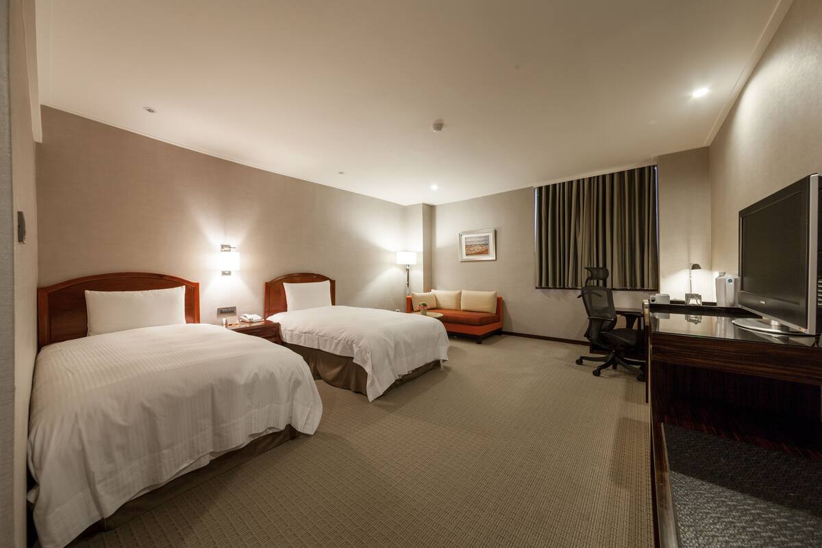 Habitación de hotel con dos camas, un escritorio con televisor y una silla.