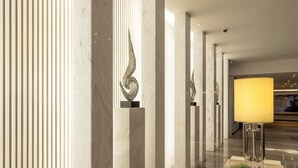 Una hall moderna con colonne in marmo, una scultura decorativa, un'esposizione di fiori e una lampada da terra.
