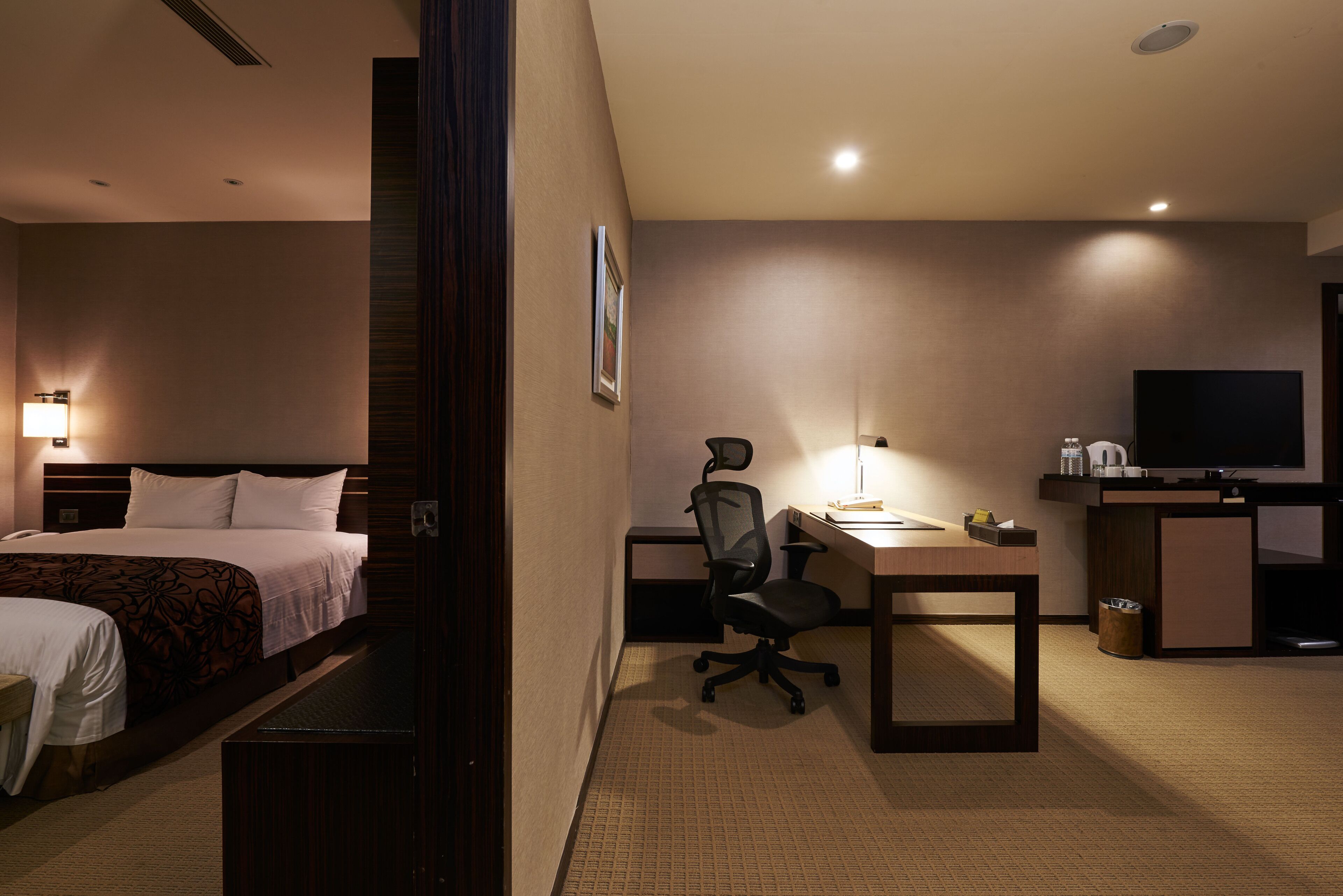 A hotel room with a bed, desk, chair, television, and a small kitchenette.