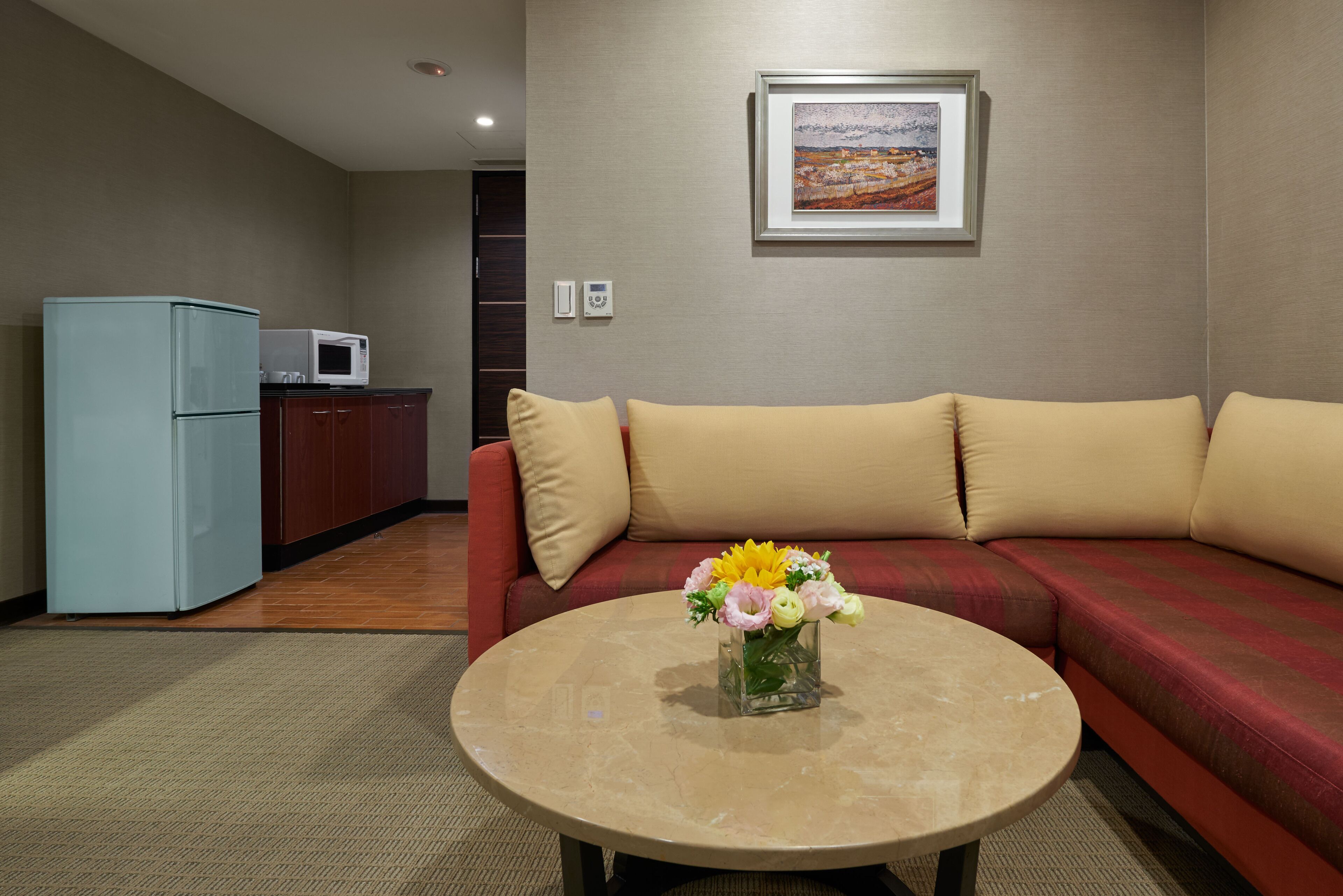 A living room with a sofa, a coffee table with a vase of flowers, a microwave, and a refrigerator.