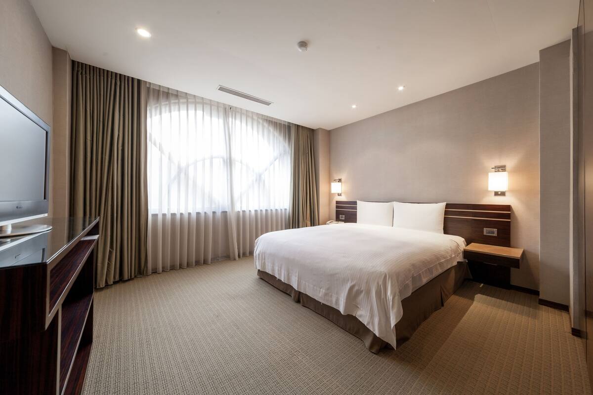 Una habitación de hotel con una cama grande, televisión, escritorio y lámpara.