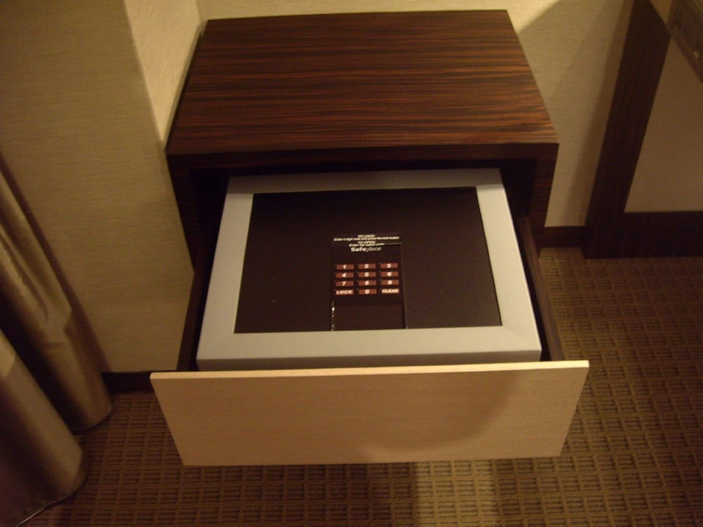 Una habitación de hotel con una mesita de noche de madera, una caja fuerte y suelo alfombrado.