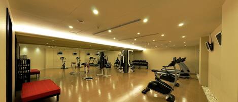 Un gimnasio con equipo de ejercicio, una banca roja y un espejo grande.