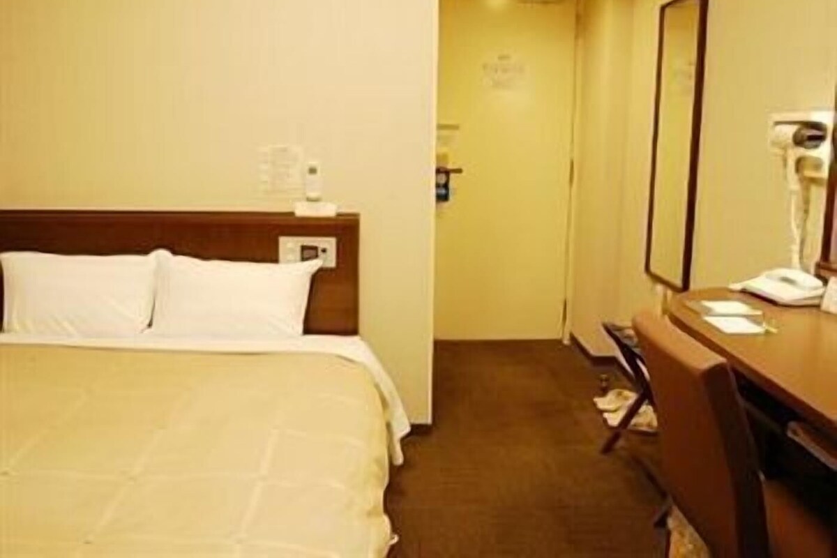 A hotel room with a bed, a desk, a chair, a mirror, and a telephone.