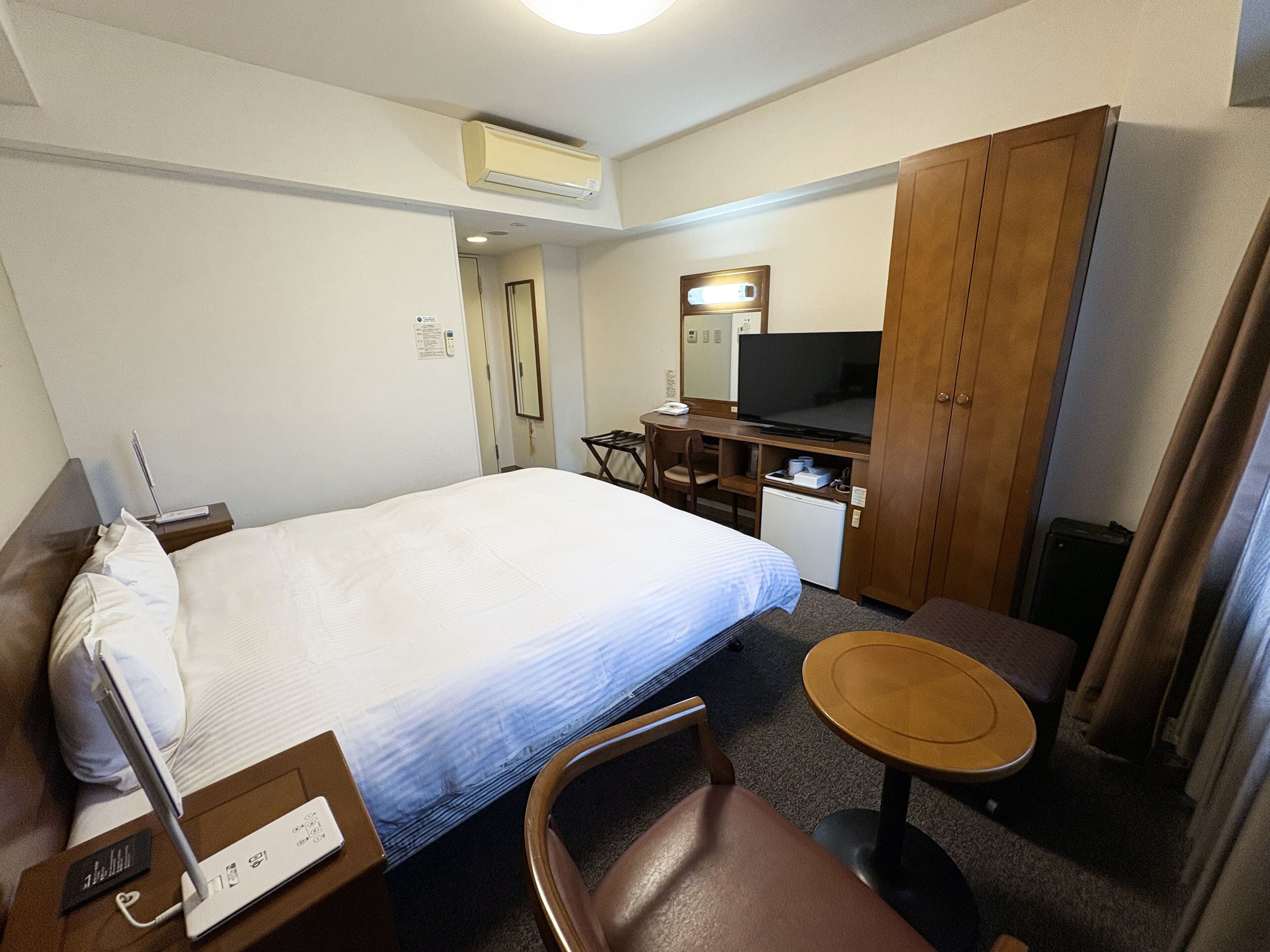 Una habitación de hotel con cama, escritorio, computadora, televisor y refrigerador pequeño.