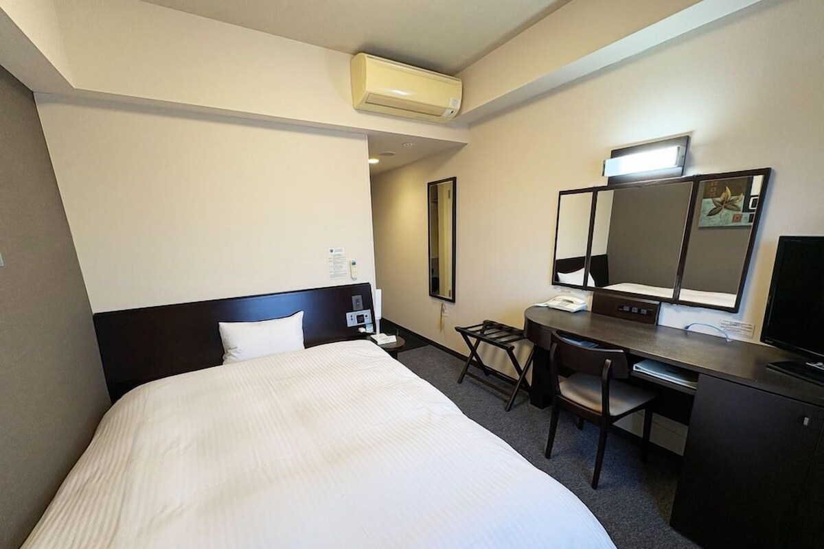 A hotel room with a bed, desk, chair, and a large mirror.