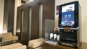 Quarto moderno com sofá, mesa, máquina de café e televisão exibindo um menu.