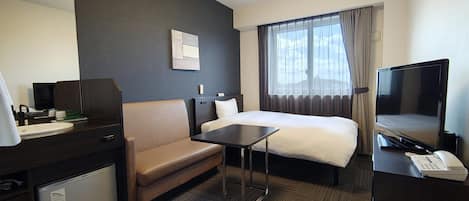 Habitació d'hotel amb un llit, una escriptori, una cadira, un televisor i una cuineta petita.