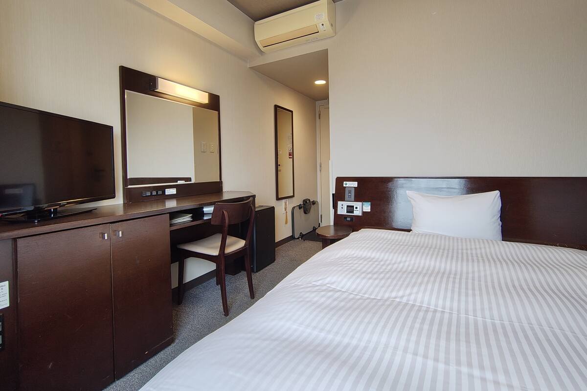 Une chambre d’hôtel équipée d’un lit, d’un bureau, d’une chaise, d’une télévision, d’un miroir et d’un appareil de climatisation.