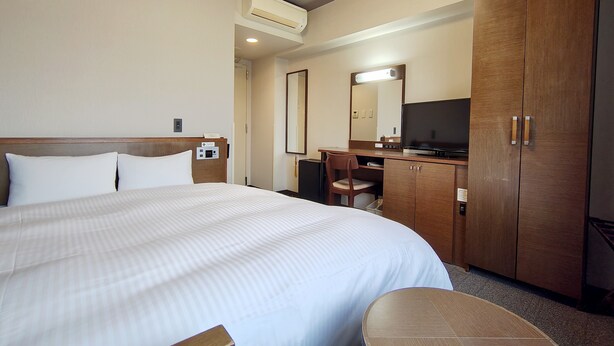 Quarto de hotel com uma cama grande, uma escrivaninha, uma cadeira, uma televisão e um guarda-roupa.