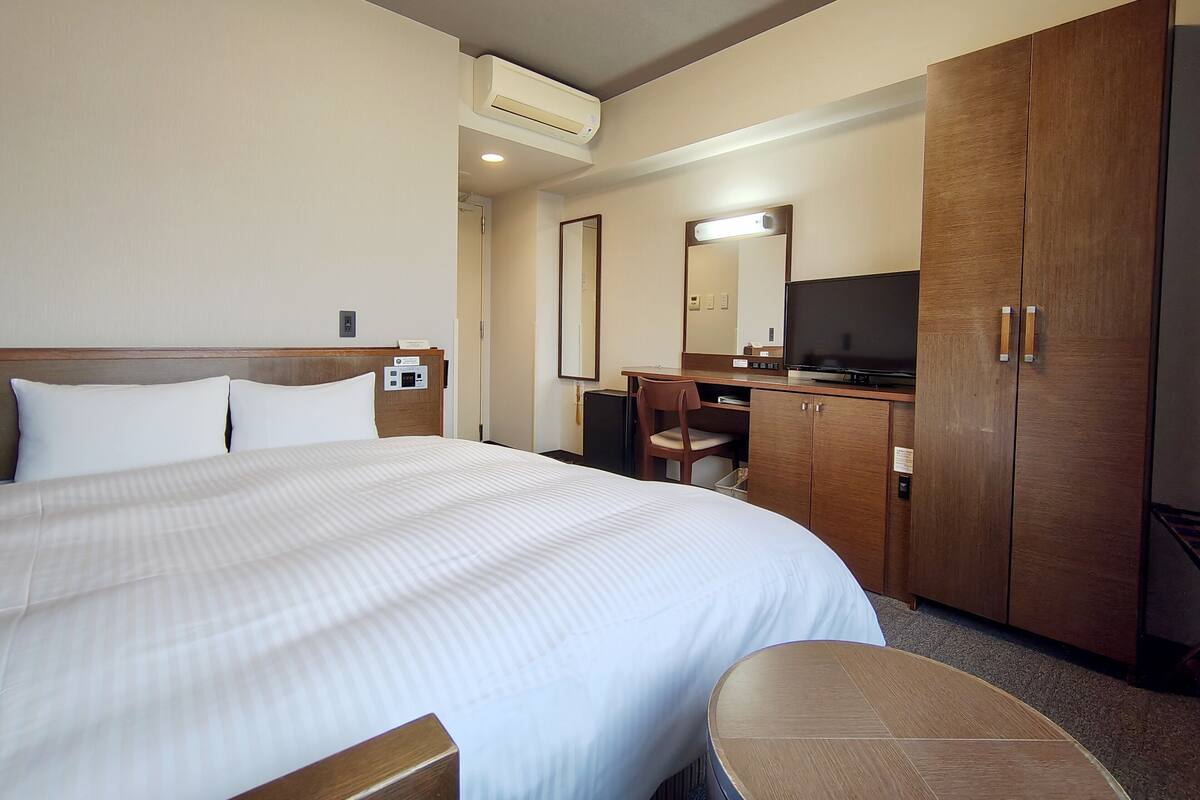 Une chambre d’hôtel avec un grand lit, un bureau, une chaise, une télévision et une armoire.