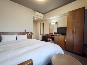 Habitación de hotel con una cama grande, un escritorio, una silla, un televisor y un armario.