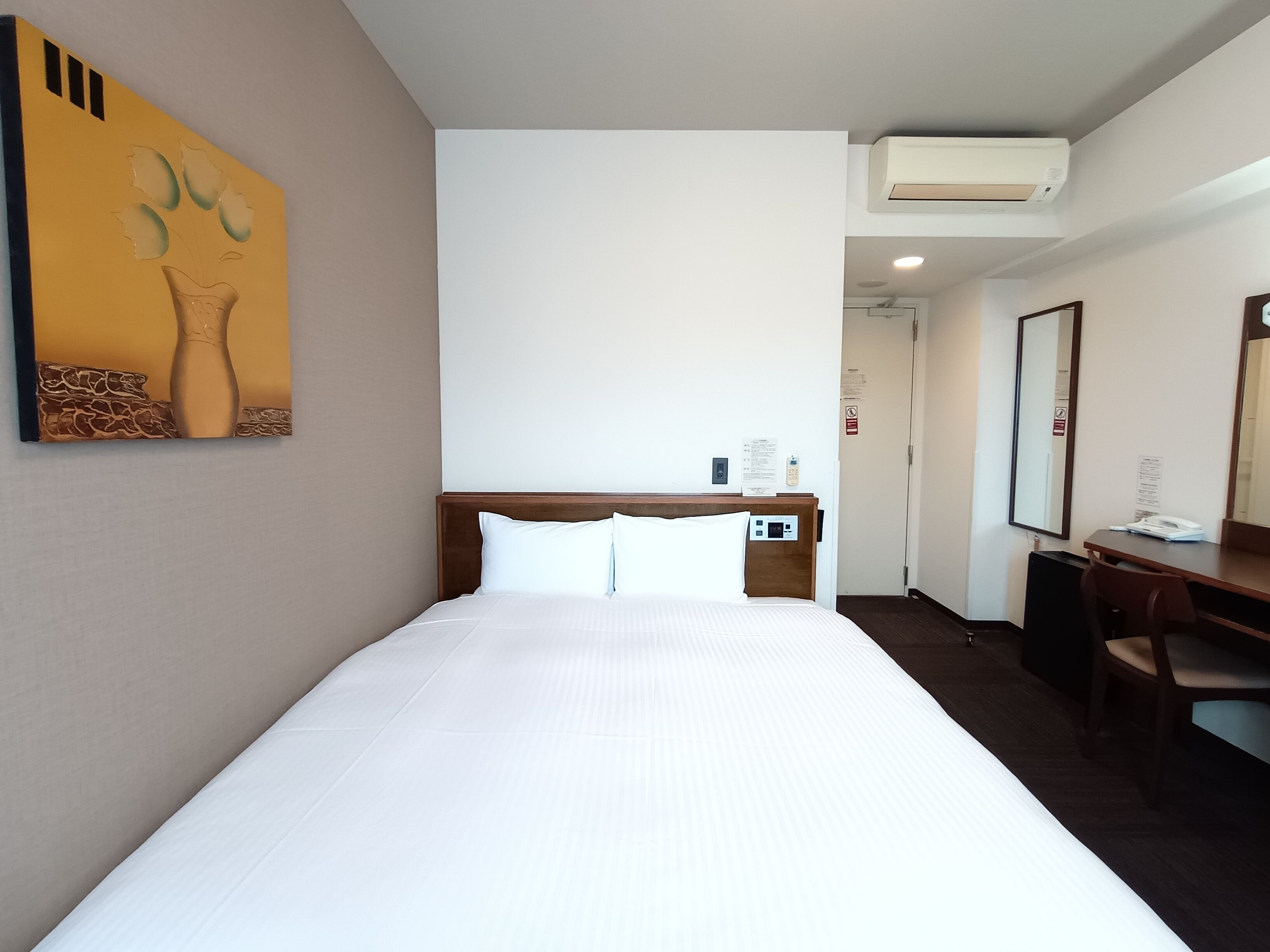 Una habitación de hotel con una cama grande, un escritorio, una silla, un espejo y un aire acondicionado instalado en la pared.