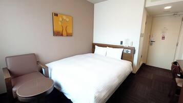 Et hotelværelse med seng, stol, lille bord, et billede på væggen og en dør med et skilt.