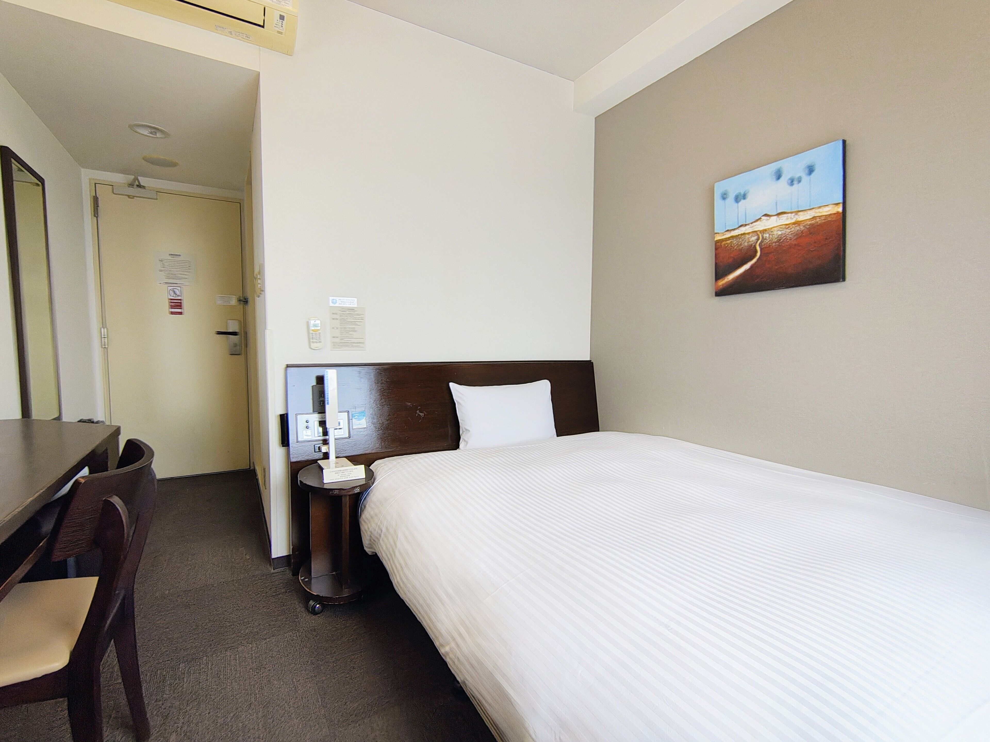 Une chambre d’hôtel avec un lit, un bureau, une chaise, une table de chevet et un tableau au mur.