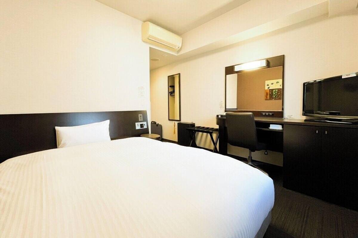 Una habitación de hotel con una cama grande, un escritorio, una silla, un televisor y un espejo.