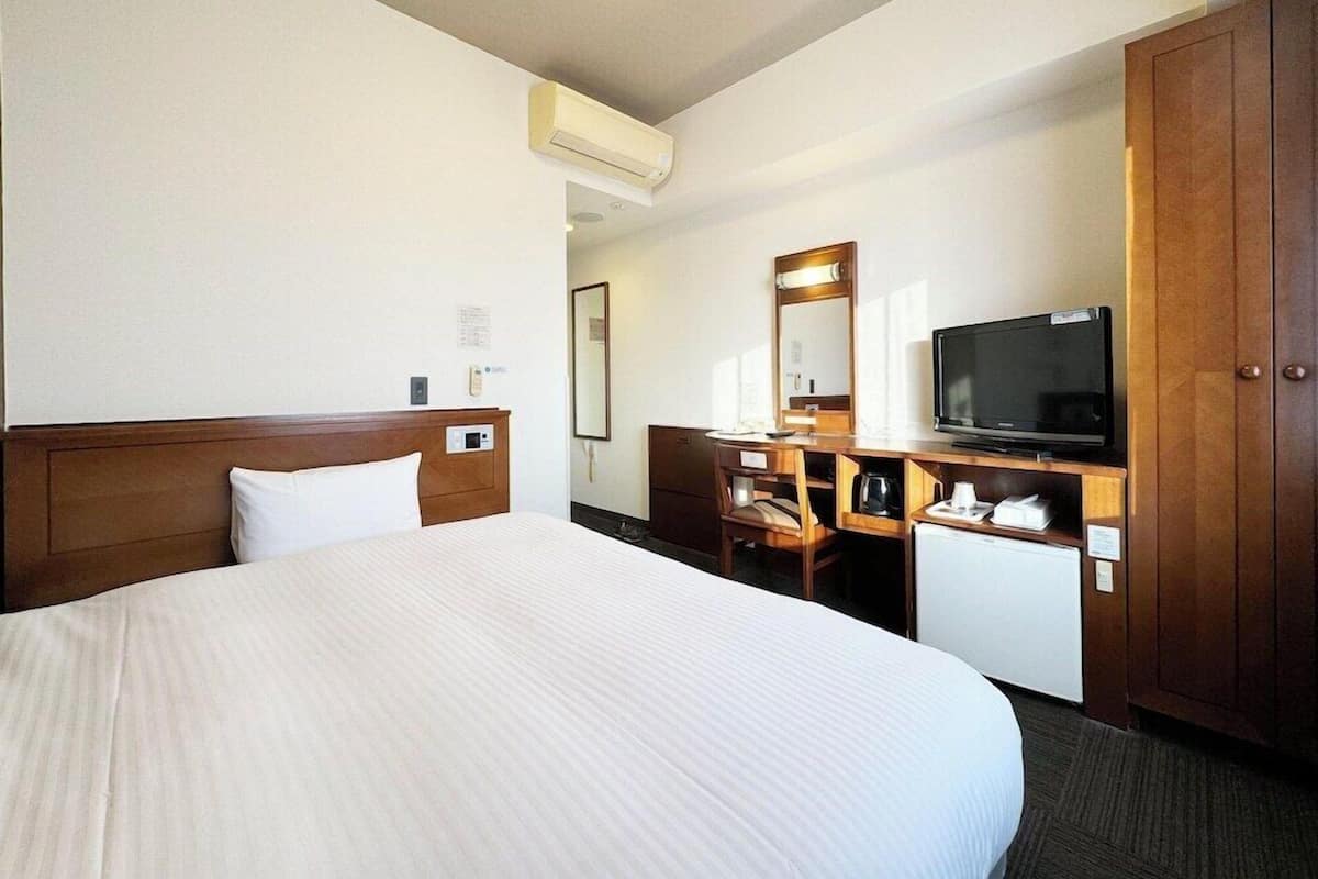Una habitación de hotel con una cama grande, un escritorio con televisor, un armario y un equipo de aire acondicionado.