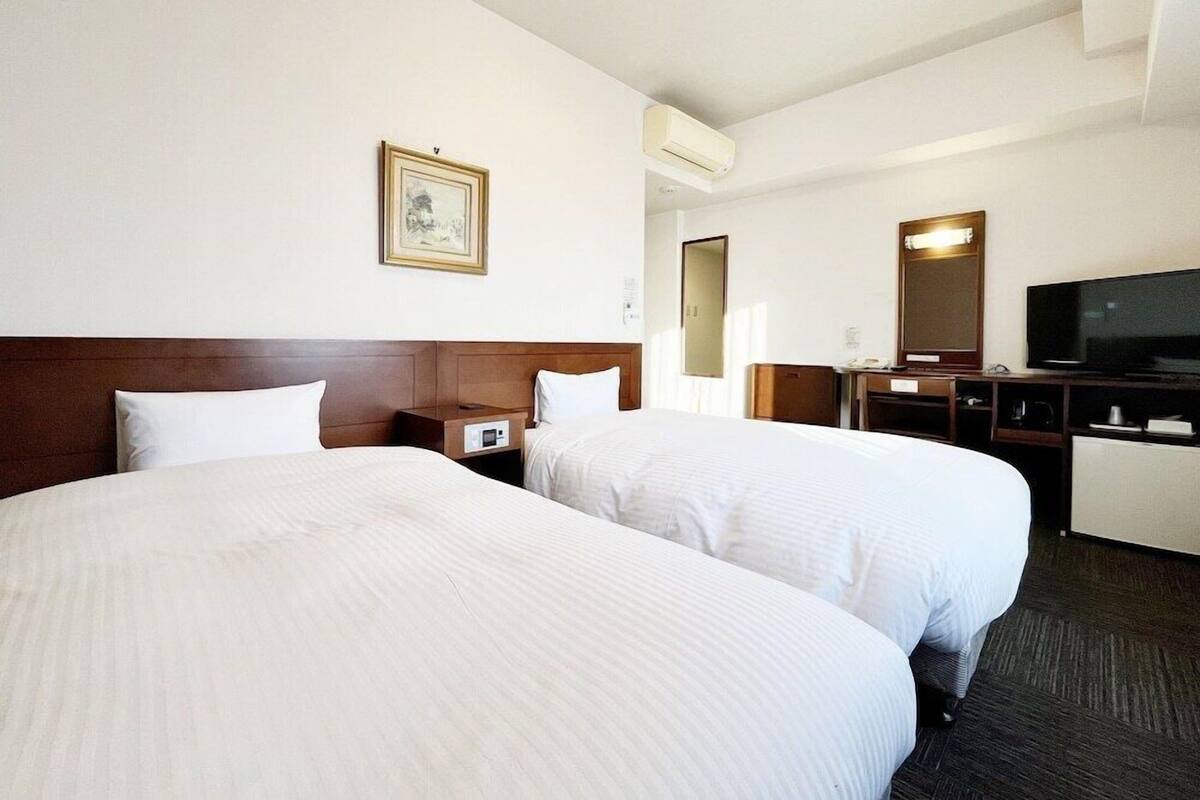 Una habitación de hotel con dos camas, televisión, escritorio y espejo.