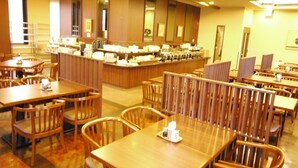 Un'area ristorazione in hotel con tavoli e sedie in legno, un banco buffet e quadri appesi alle pareti.